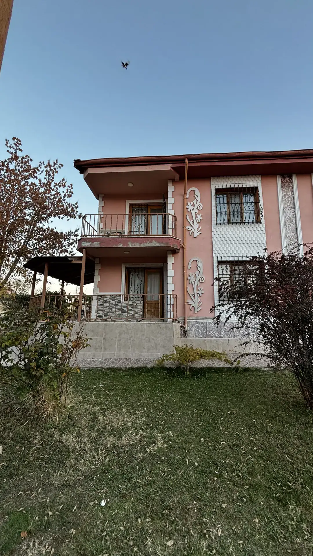 Bahçeye bakan, balkonlu ve beyaz kabartma süslemeli cephe ile önündeki çimenlik