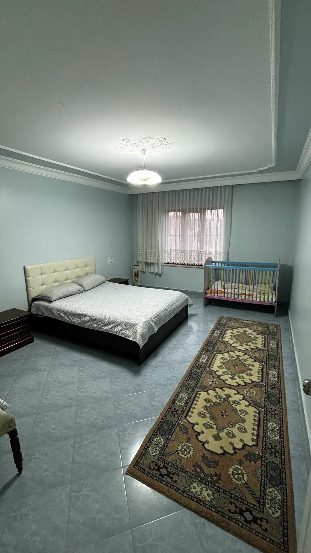 Çift kişilik yatak, bebek karyolası ve desenli yolluk halıyla ebeveyn odası