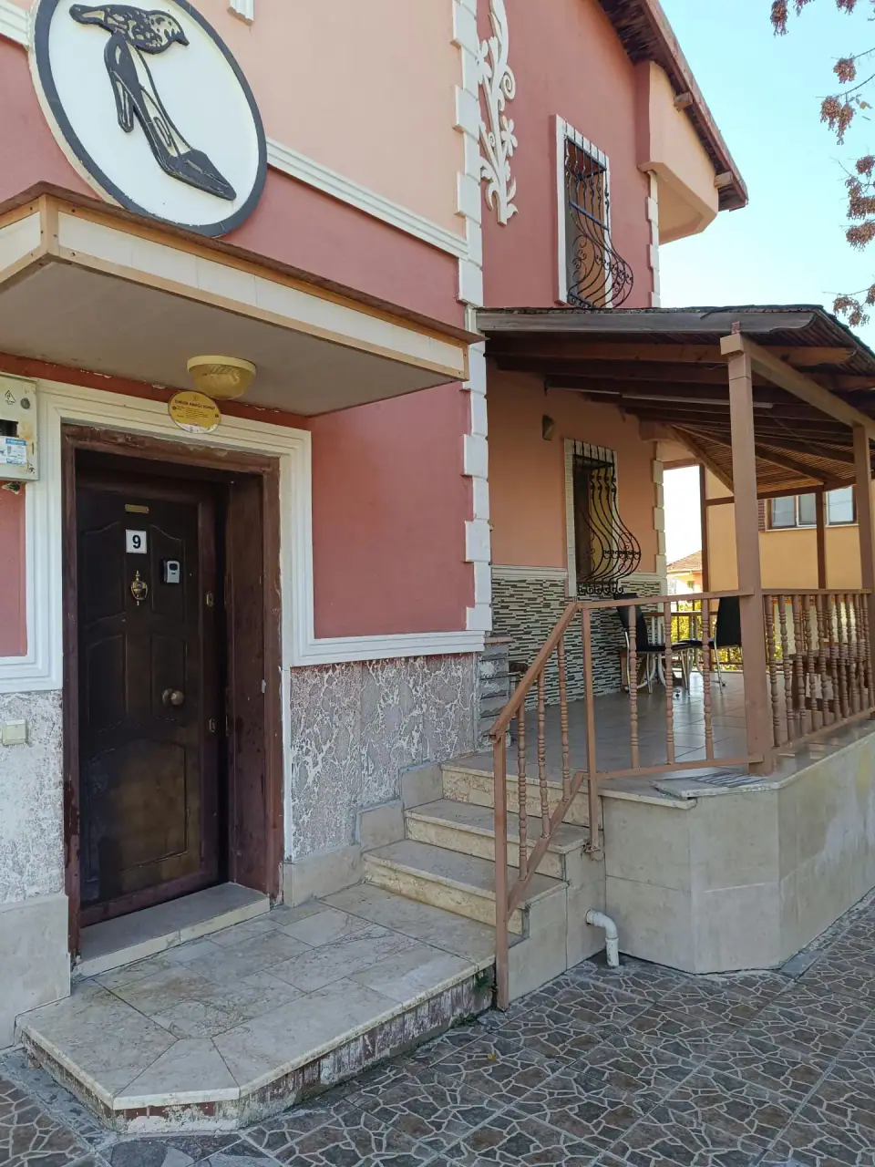 The entrance door in daylight, marble steps and the timber-roofed terrace beside it