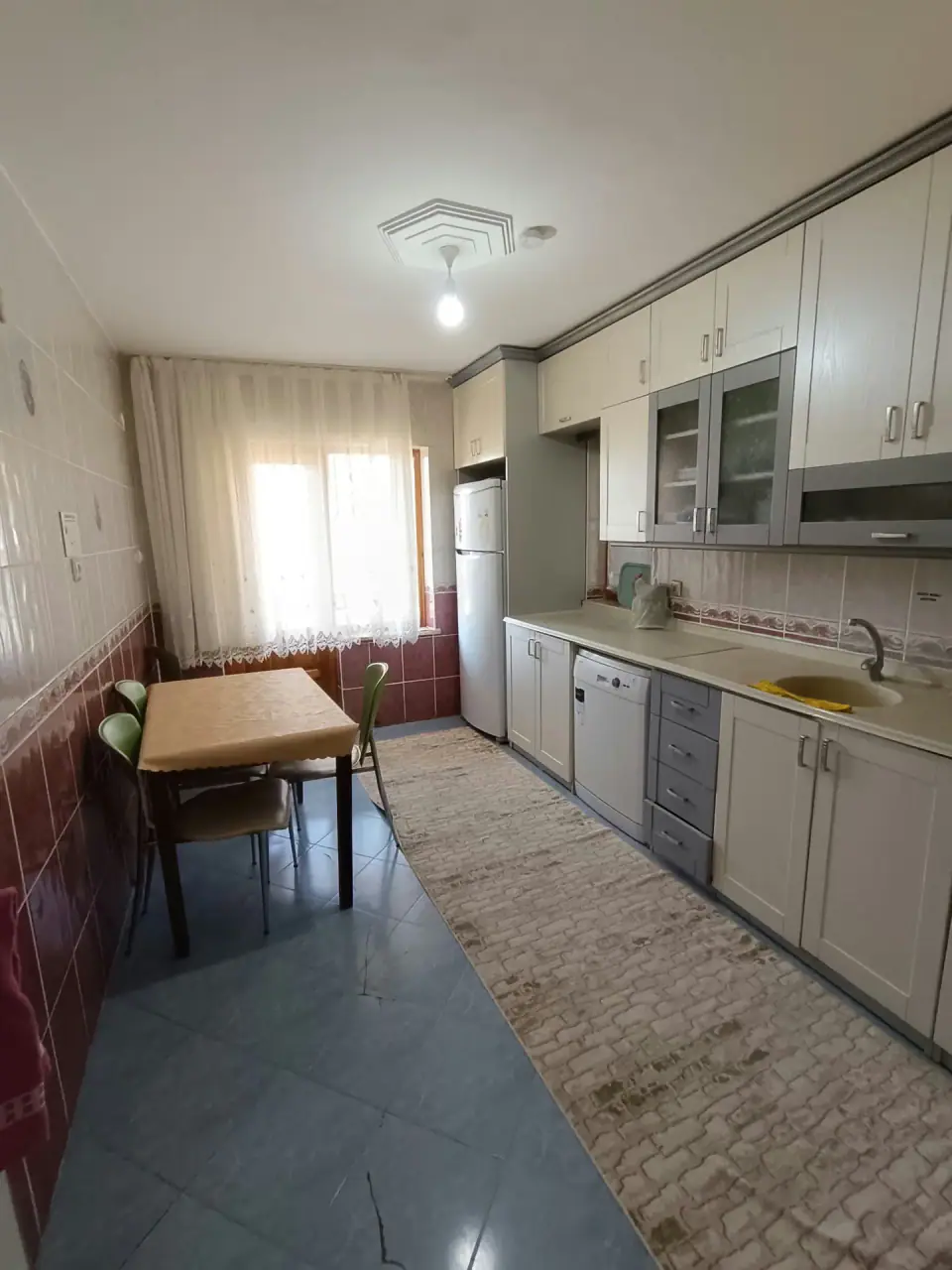A dining table by the window, a fridge, a dishwasher and a long counter in the kitchen