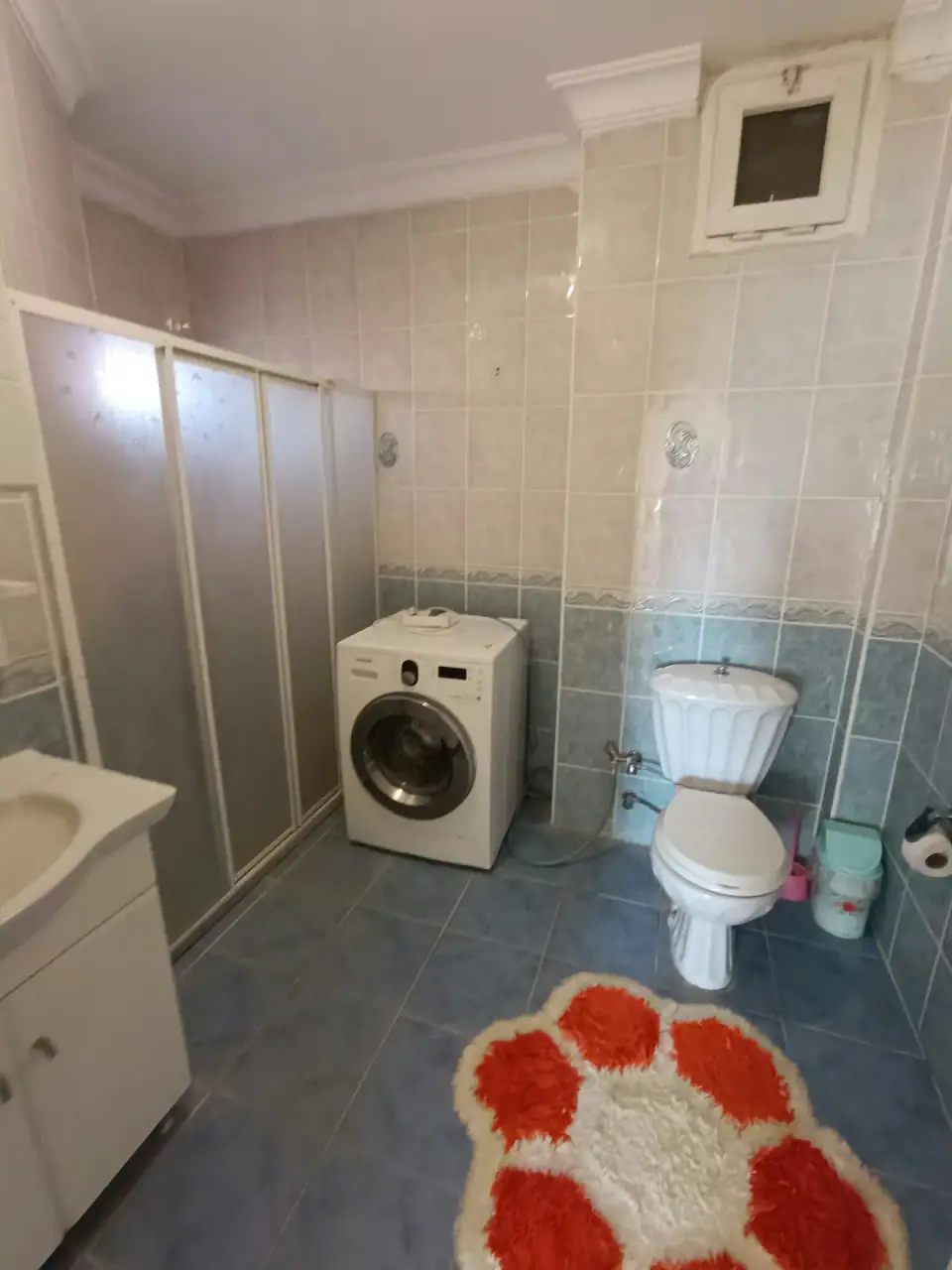 A shower cabin, a washing machine and a flower-shaped mat in the bathroom