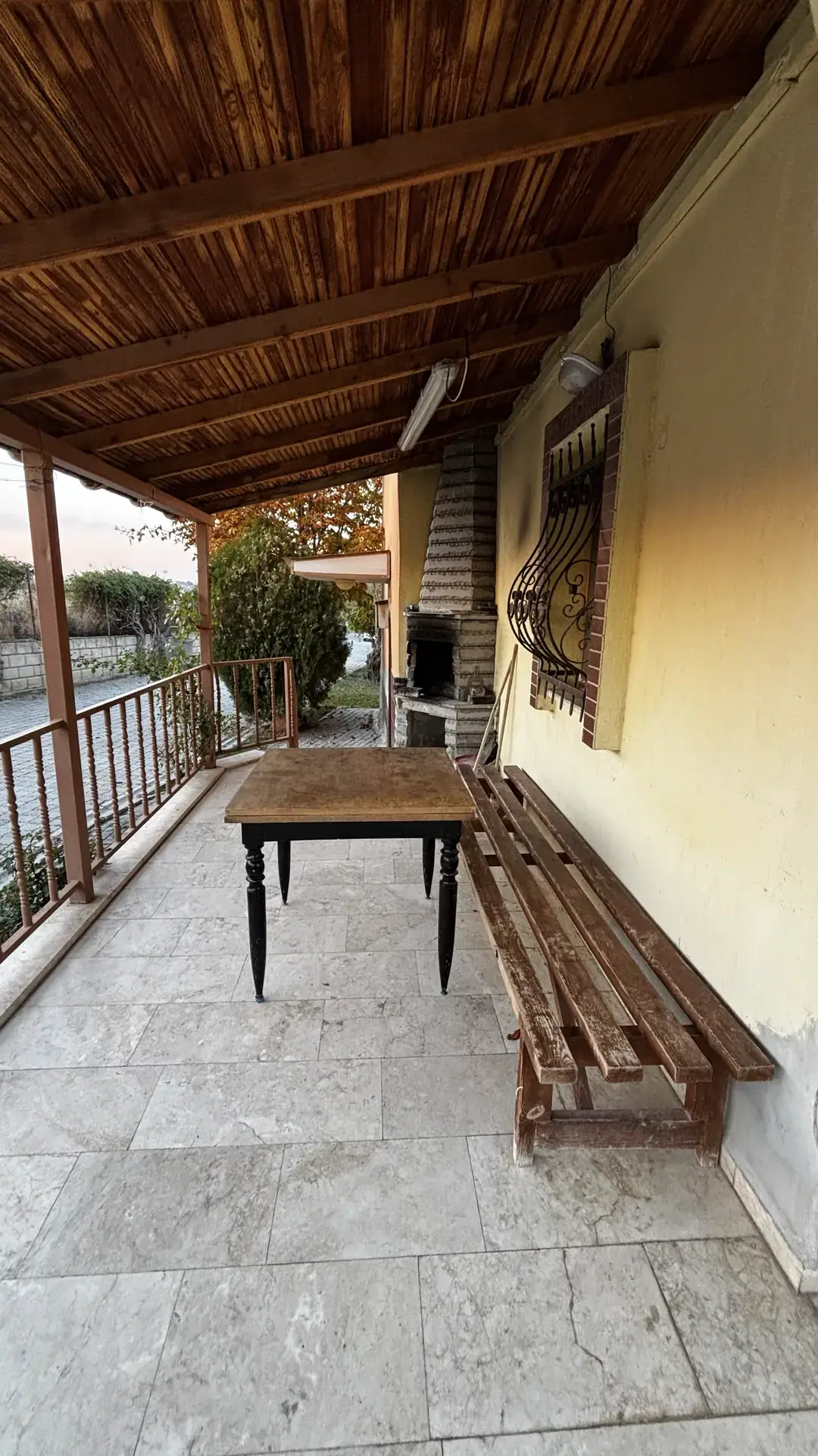 Ahşap tavanlı terasta yemek masası, uzun bank ve taş mangal