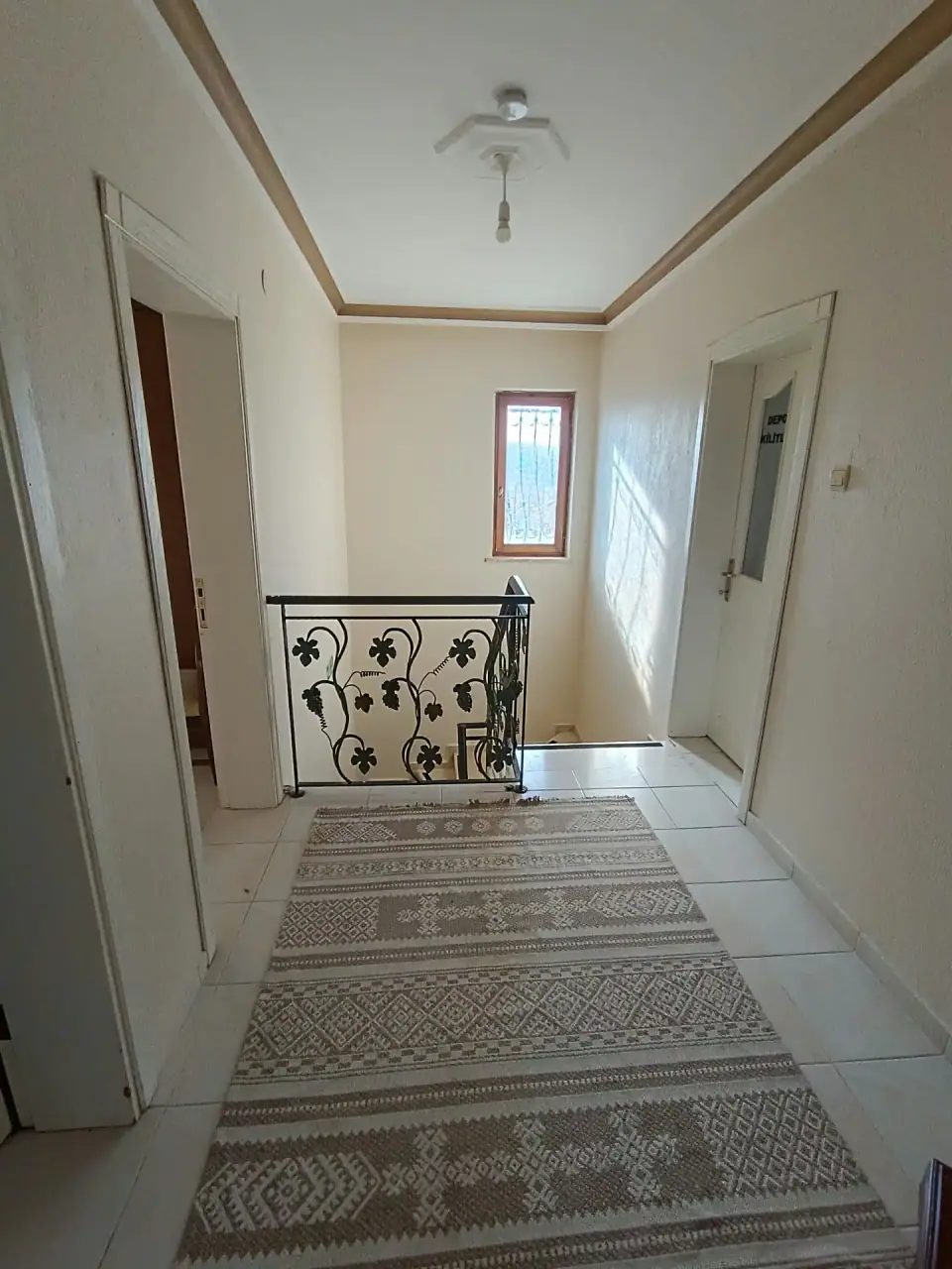 The upstairs hall in daylight with a kilim runner and wrought-iron balustrade