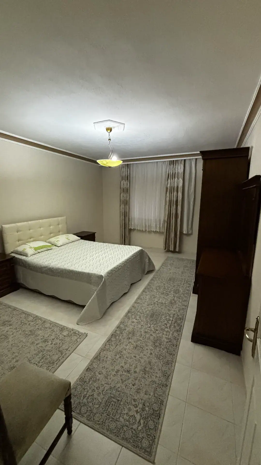 A double bed with a tufted headboard, a dark timber wardrobe and long curtains